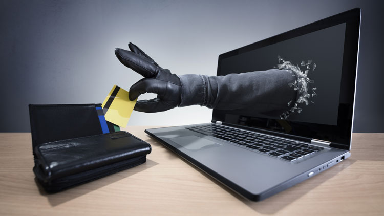 Aus einem aufgeklappten Laptop kommt eine Hand im Lederhandschuh, die eine Kreditkarte aus einem Geldbeutel herausnimmt; Copyright Panthermedia