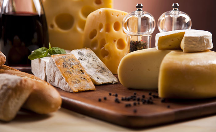 Servierbrett mit verschiedenen Käsesorten, Brot, Pfeffer und einer Karaffe Wein.