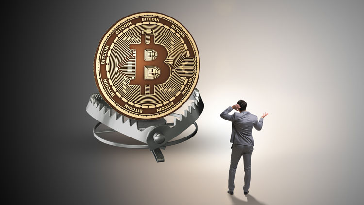 Das Bild zeigt einen ratlosen Mann, der auf eine übergroße Bitcoin-Münze schaut, die in einer Schnappfalle liegt; Copyright Panthermedia