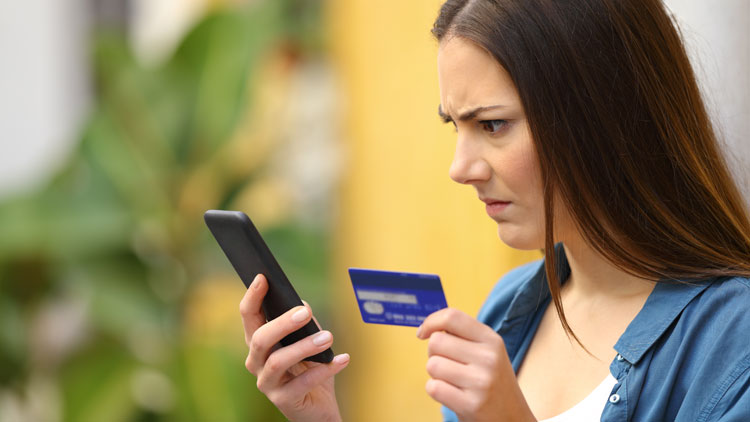 Ärgerliche Frau blickt auf Kreditkarte in ihrer Hand und ein Handy, Copyright Panthermedia