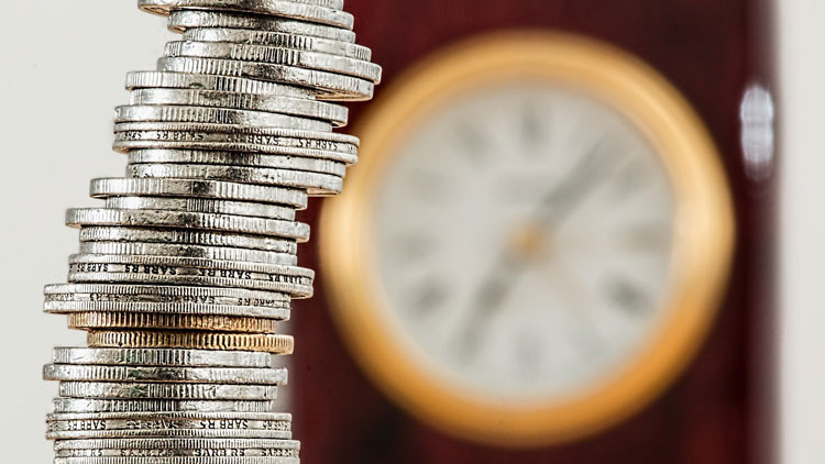 Das Bild zeigt einen schiefen Turm aus Münzen vor einer Wanduhr, Copyright Pixabay