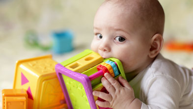 Baby, das auf dem Bauch liegt und ein buntes Plastikspielzeug mit dem Mund erkundet; Copyright Panthermedia