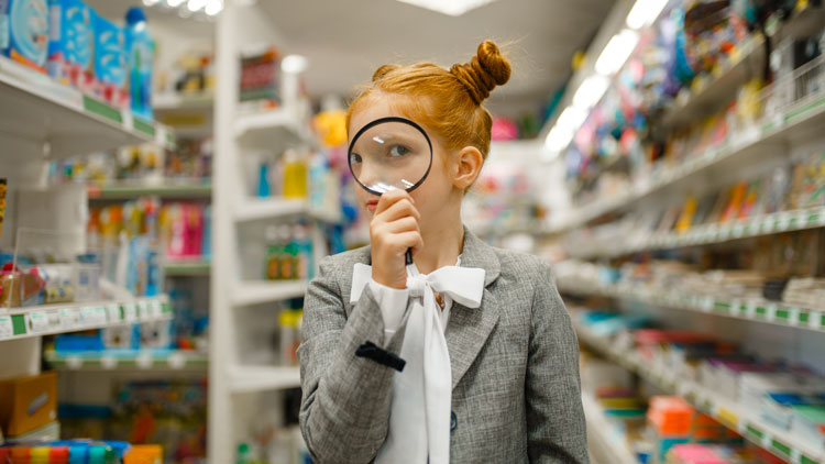 Mädchen steht im Gang eines Supermarktes und schaut durch eine Lupe; Copyright Panthermedia