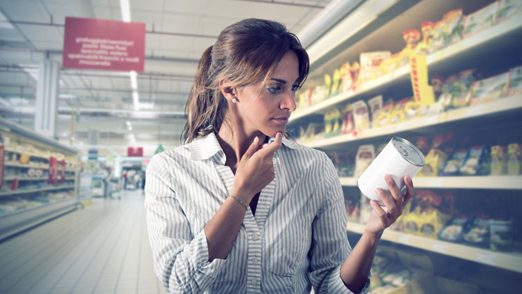 Junge Frau im Supermarkt schaut prüfend auf ein Dosenetikett; Copyright Panthermedia