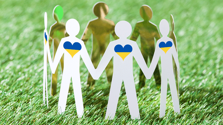 Ein Kreis aus Papierfiguren mit Herzen in den Farben der ukrainischen Flagge stehen auf einer Wiese und halten sich an den Händen; Copyright Panthermedia